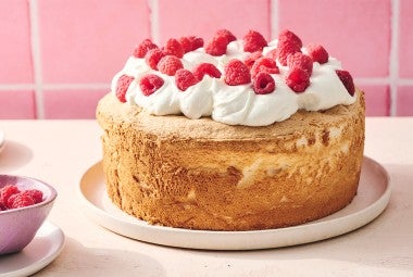 A compelte Gluten-Free Angel Food Cake topped with whipped cream and raspberries