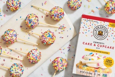 Confetti Cake Pops on a countertop with a box of confetti cake and cupcake mix made by King Arthur Baking in the frame. Seen from above.