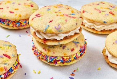 Confetti Whoopie Pies stacked on a counter with sprinkles decorating the filling around the outside of the whoopie pies.